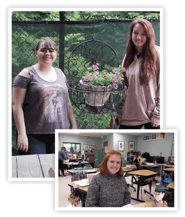 Two Students Standing Either Side a Hanging Potted Plant and a Student Sitting at a Table